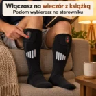 Wieczór na kanapie przy lampie: dłoń naciska sterownik, nogi podkulone, obok kubek i książka